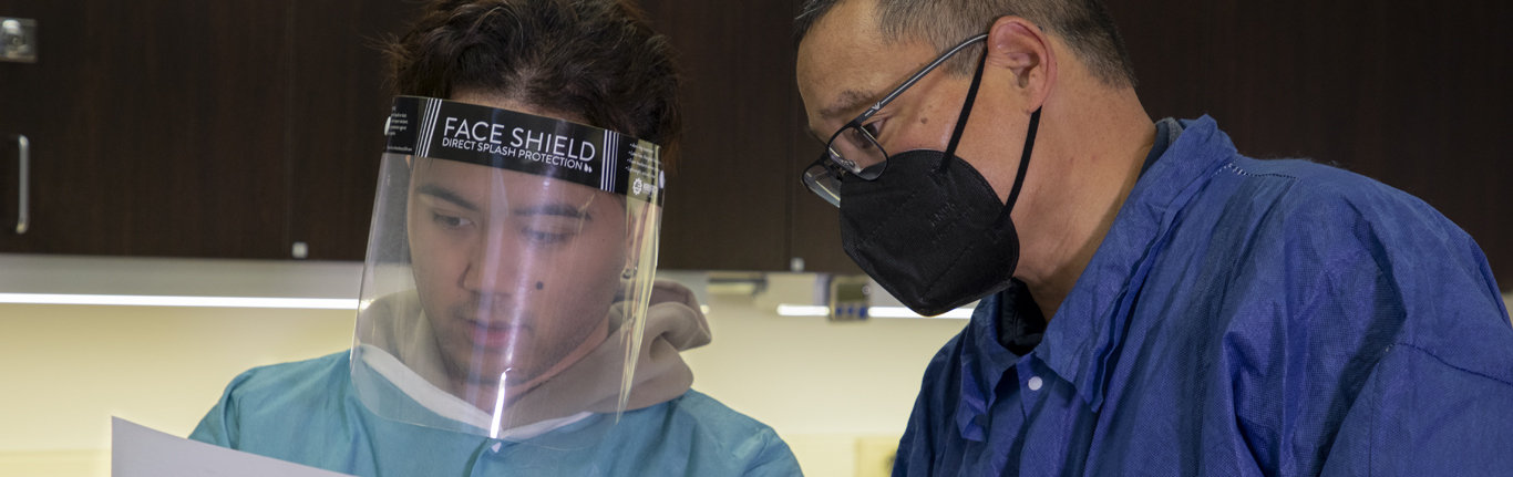 CLS instructor with student in lab coats and splash masks. 