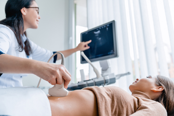 Close up of doctor using sonography machine with digital monitor. Medical specialist does ultrasound diagnostic to pregnant female patient. Modern clinic or medical center with advanced equipment.