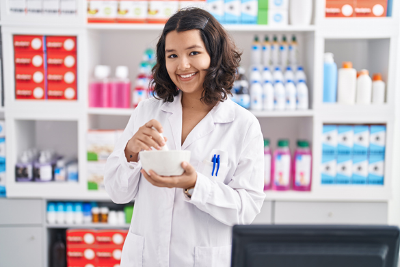 Young woman pharmacist smiling confidently while mixing medicine at pharmacy.