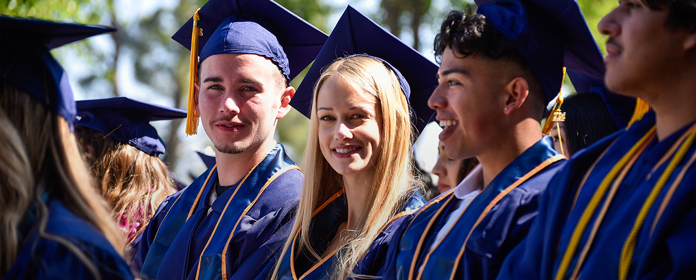 Students in caps and gowns smile during commencement.)