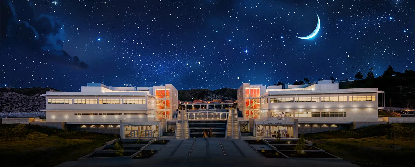 Modern, brightly lit campus buildings at night beneath a star-filled sky with a crescent moon, viewed symmetrically from a central walkway.