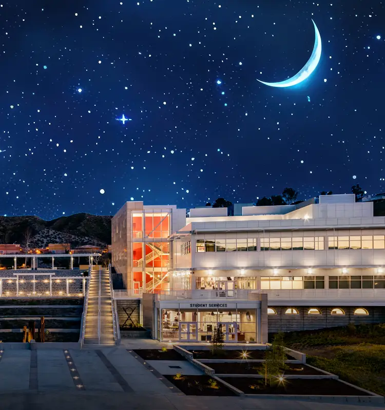 Modern, brightly lit campus buildings at night beneath a star-filled sky with a crescent moon, viewed symmetrically from a central walkway.