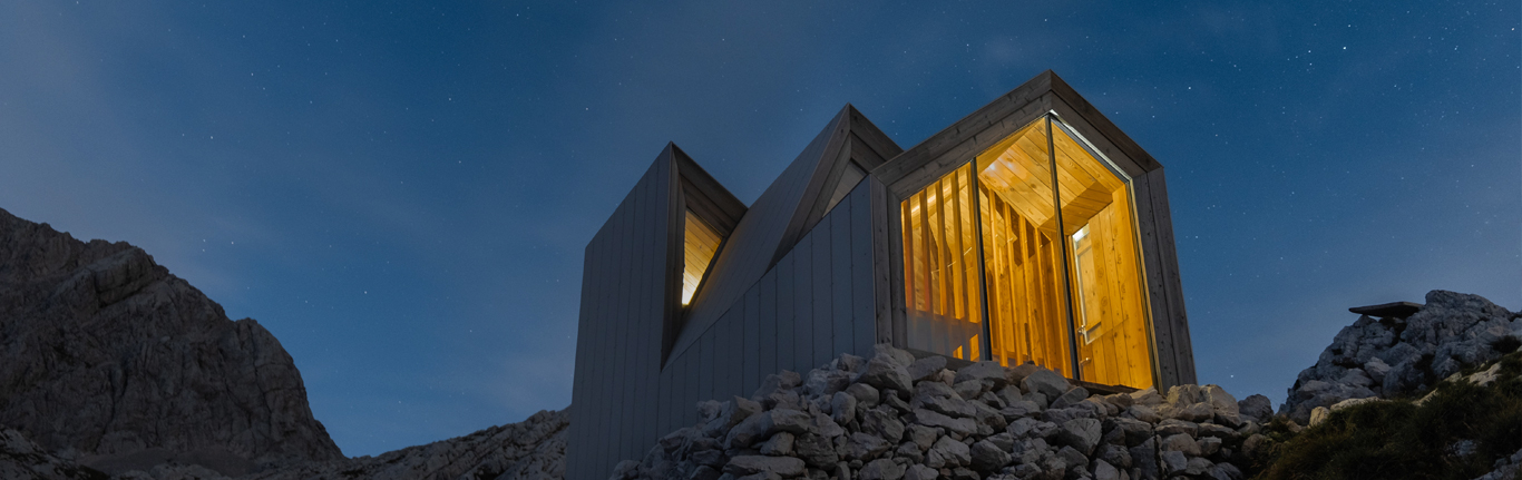 Modern home at night, with peaked roof, lit windows aglow.