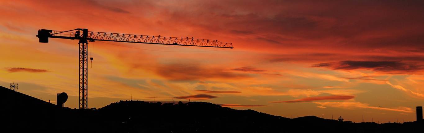 Construction site at sunset with buildings and cranes.