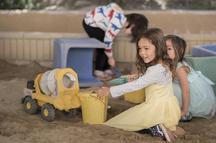 Little girls in dresses playing with truck in the sandbox at the Early Childhood Education program. 