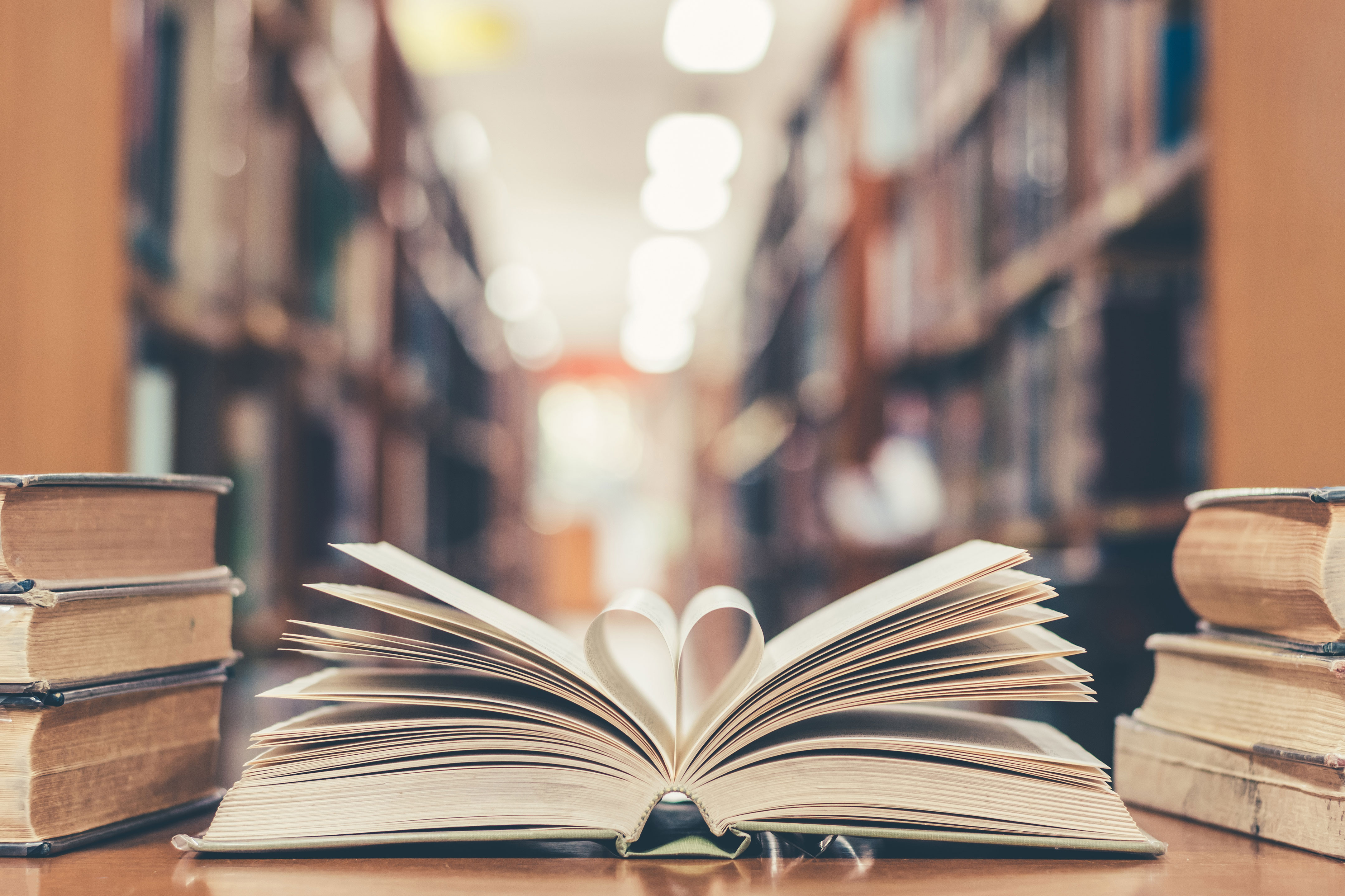 Book with open page of literature in heart shape and stack piles of textbooks on reading desk in library