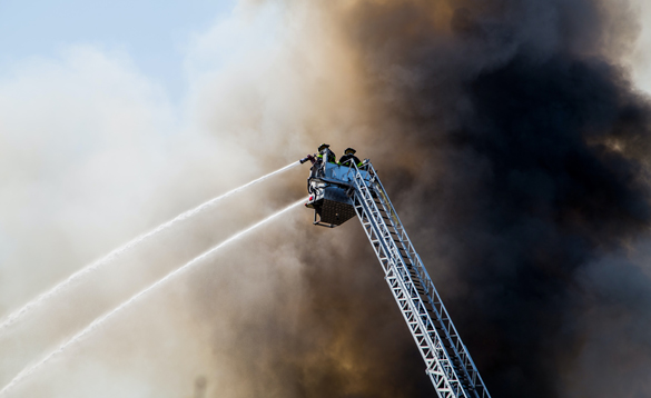 Firefighters spraying water from a tall, extended ladder.
