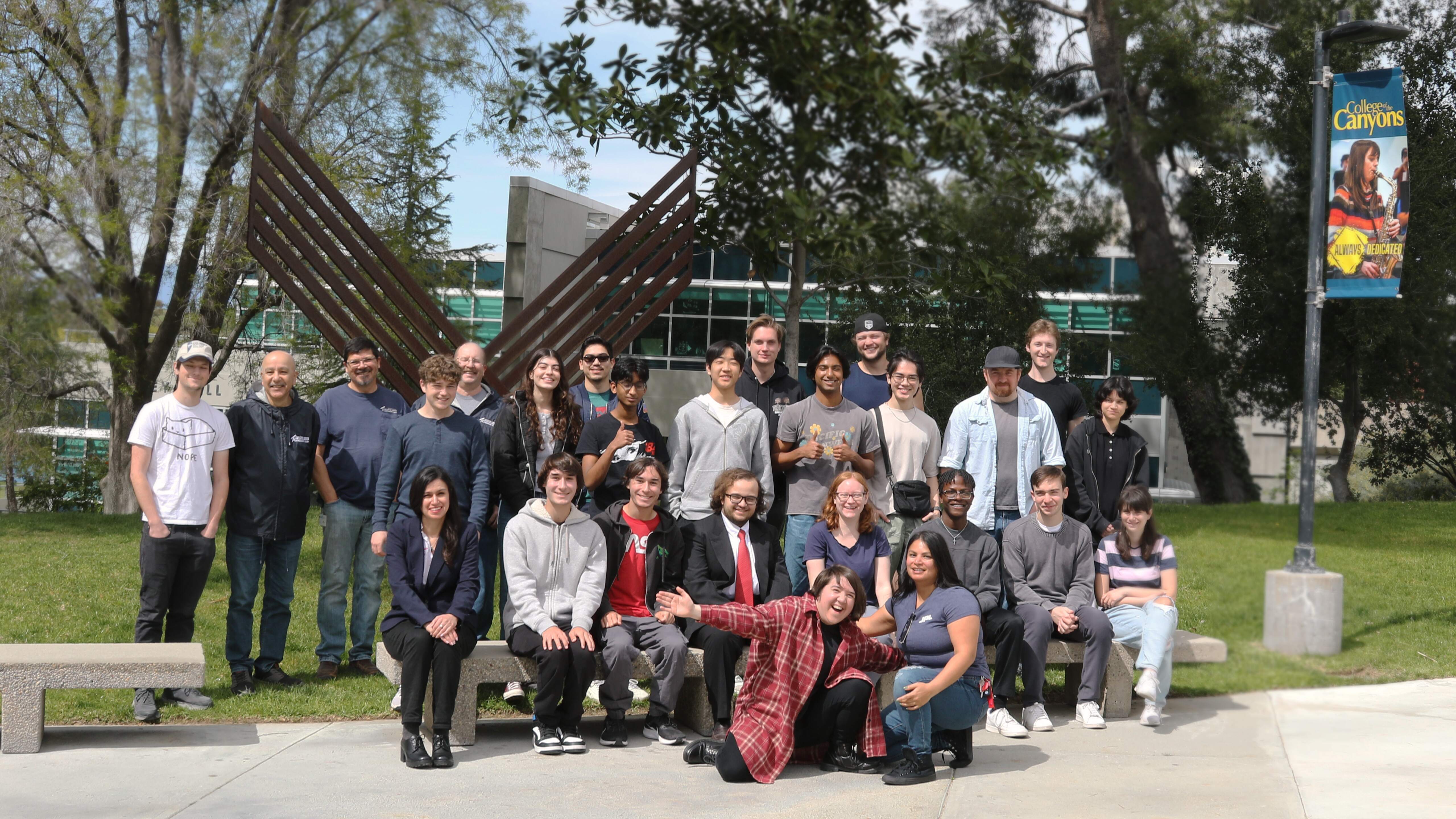the group of stem students that participate in the program stand in rows in front of a sculpture in the college honor grove