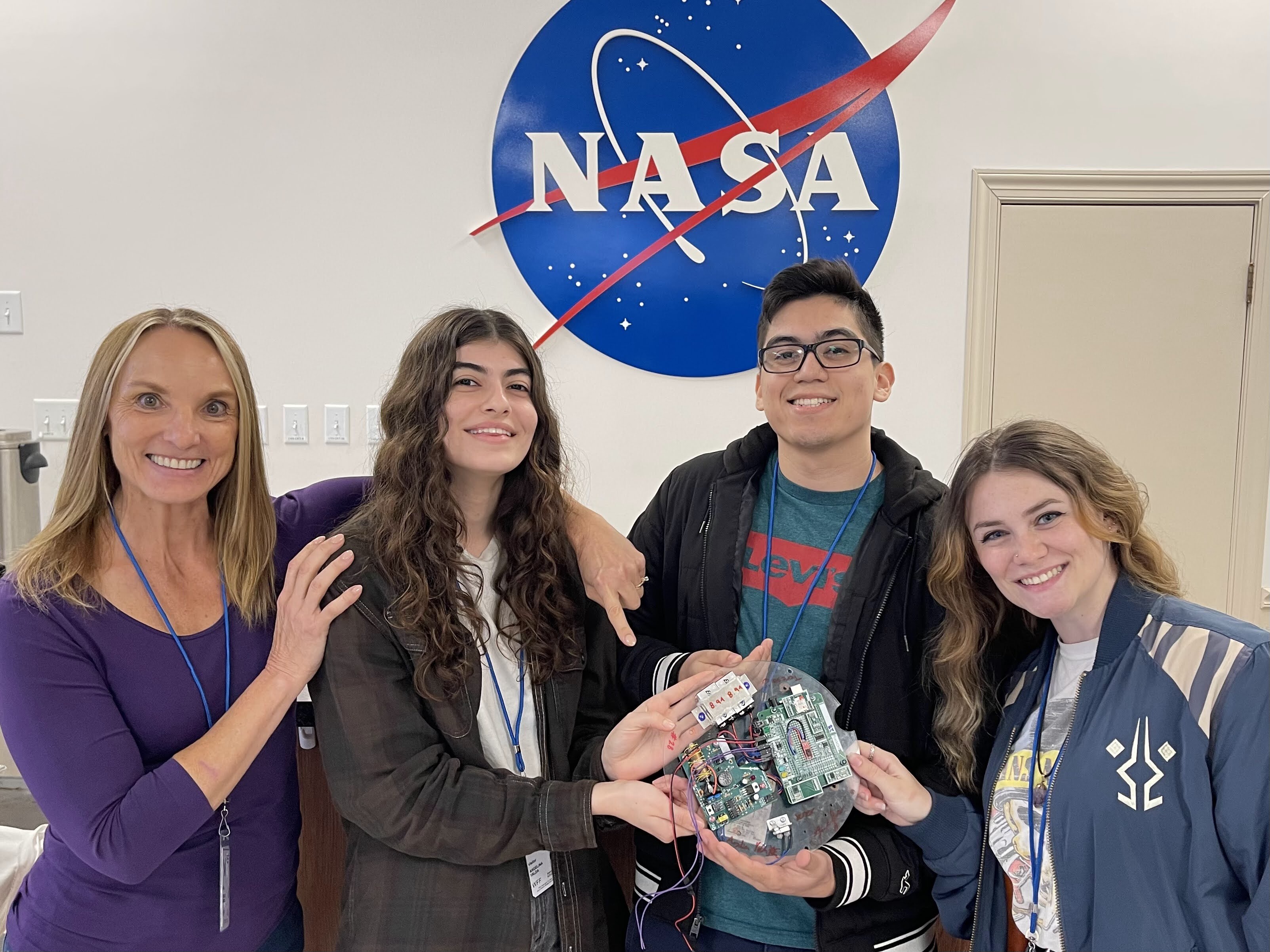 Advisor Teresa Ciardi and three students pose at NASA facility, holding the experiment they built