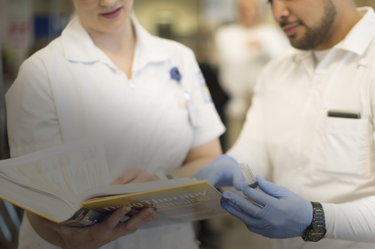 Nurses in practice lab looking at nursing book.