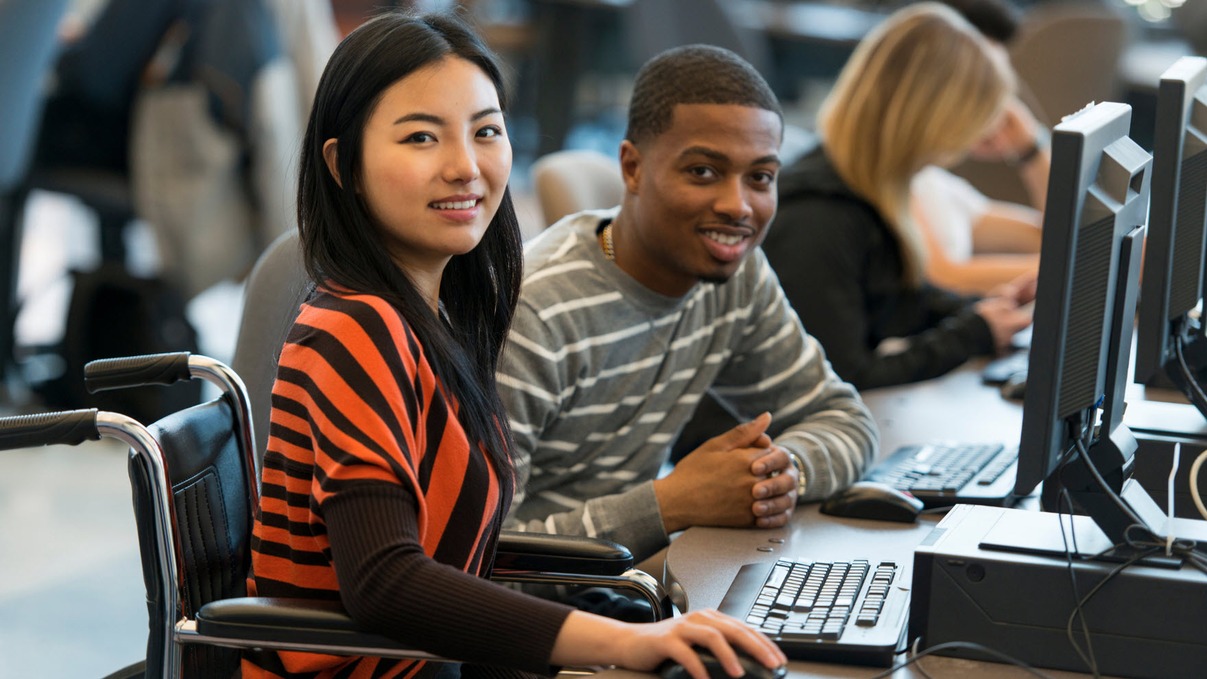two students smiling while sitting at desktop computers