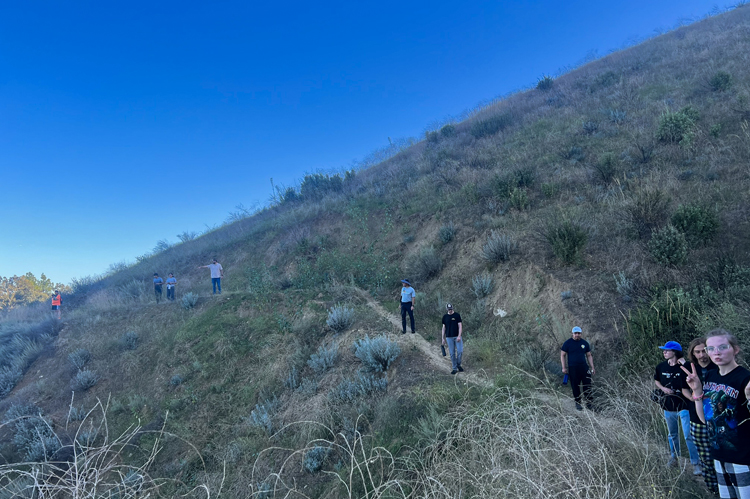 Students walking along a narrow dirt path on a hill.