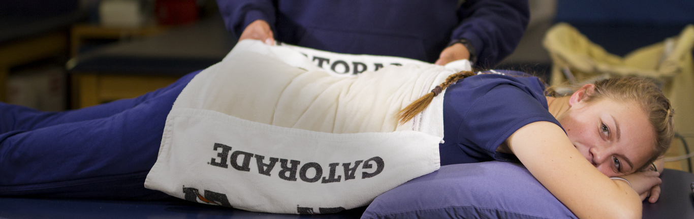 Sports Medicine faculty applying warm pad on athlete's injuried lower back. 