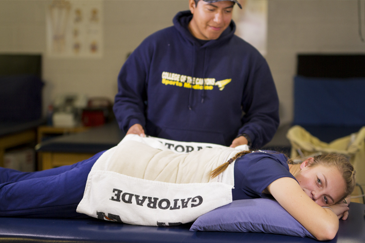 Sports Medicine faculty applying warm pad on athlete's injuried lower back. 