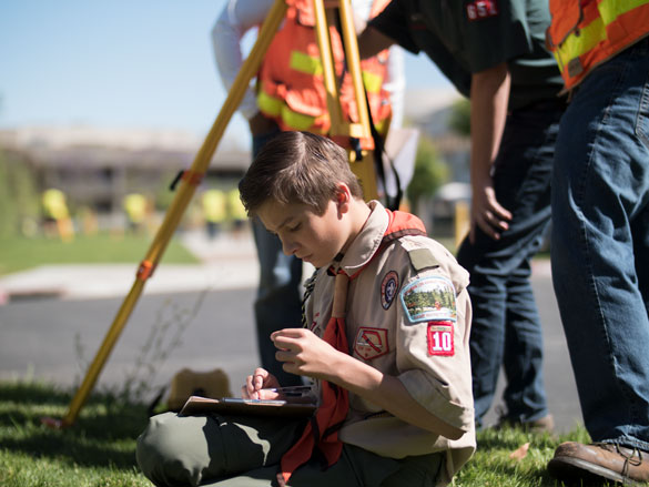 Boy Scouts look through surveying tool, with two COC Surveying instructors assisting. 