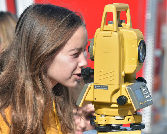 Young lady looking through a total station surveyor’s tool during the College to Career Day at COC.