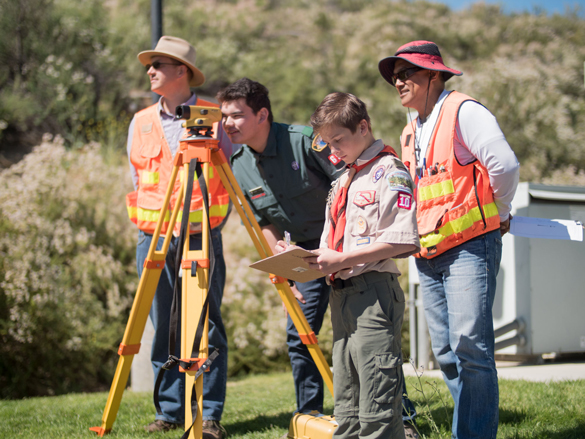 Two Boy Scouts look through surveying tool, with two COC Surveying instructors assisting.