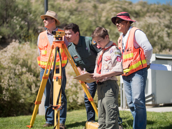 Two Boy Scouts look through surveying tool, with two COC Surveying instructors assisting. 