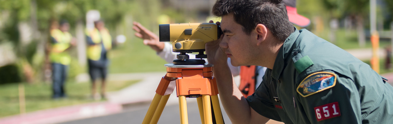 Boy Scout looking through surveying equipment. 