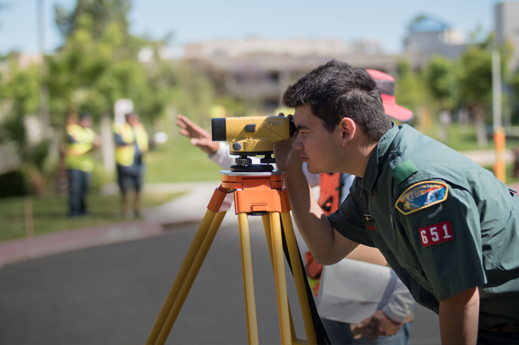 Boy Scout looking through surveying equipment. 