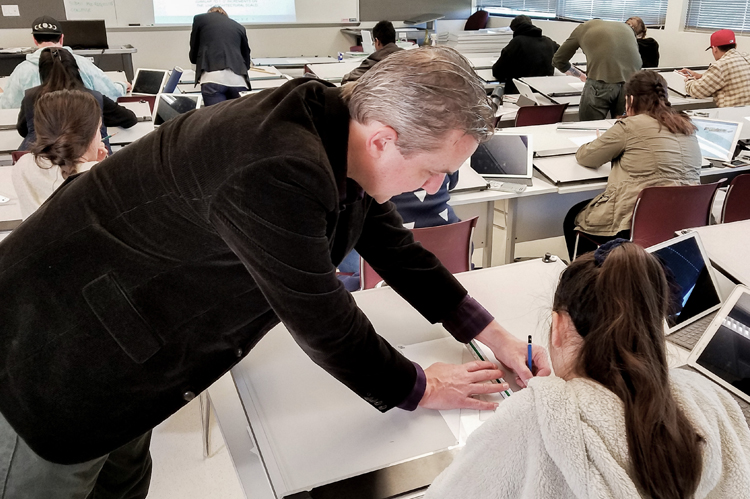 Faculty instructor in classroom helping students.